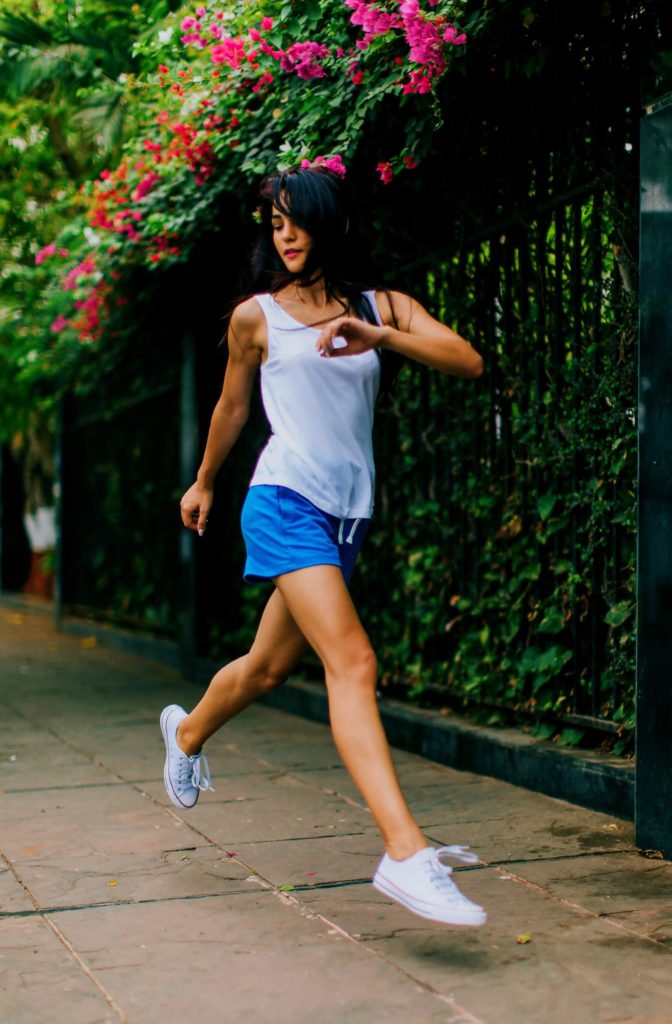 woman running on a pavement lined with hedges in bloom